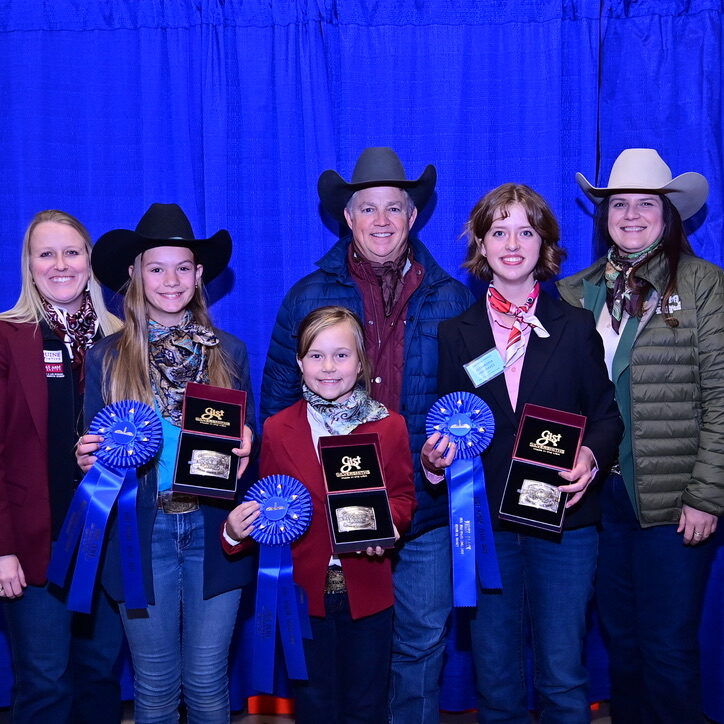 Three girls holding awards in front of blue backdrop